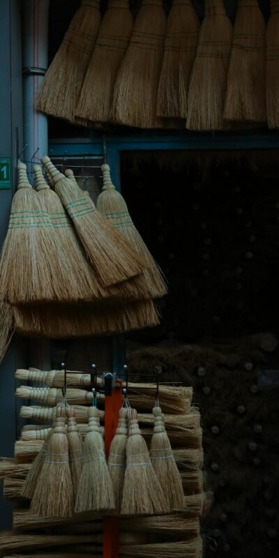 A variety of brooms arranged in a market stall, showcasing traditional craftsmanship in an urban setting.