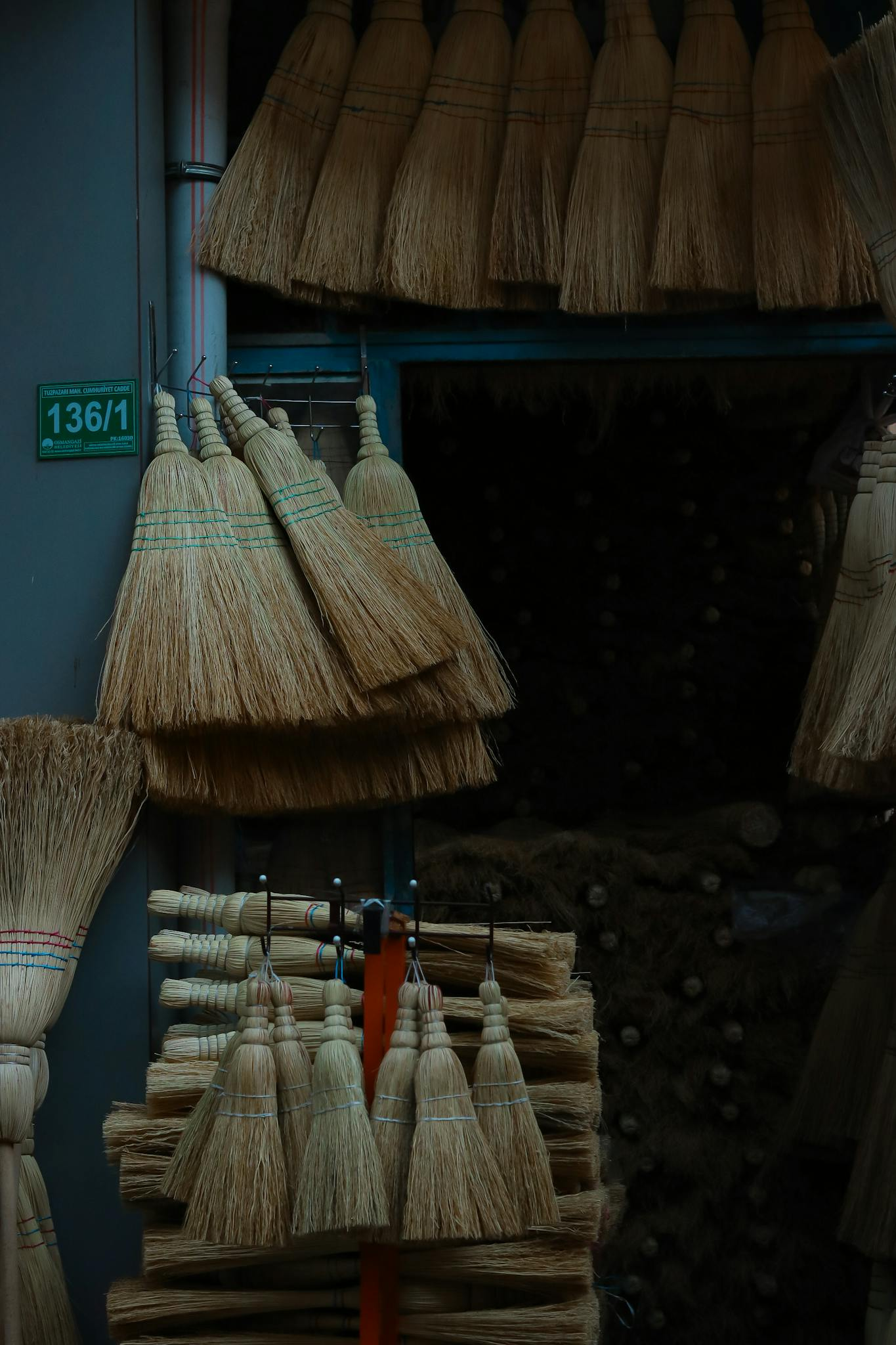 A variety of brooms arranged in a market stall, showcasing traditional craftsmanship in an urban setting.
