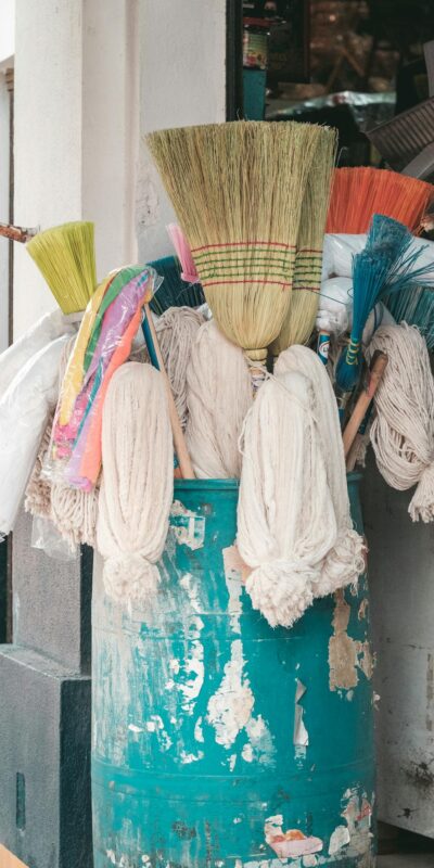A vibrant display of brooms and mops in a rustic barrel outside a store entrance.