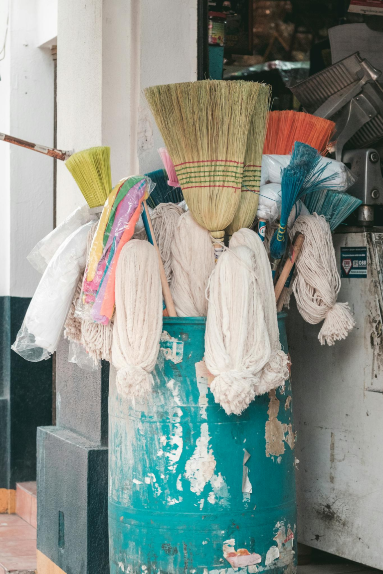 A vibrant display of brooms and mops in a rustic barrel outside a store entrance.