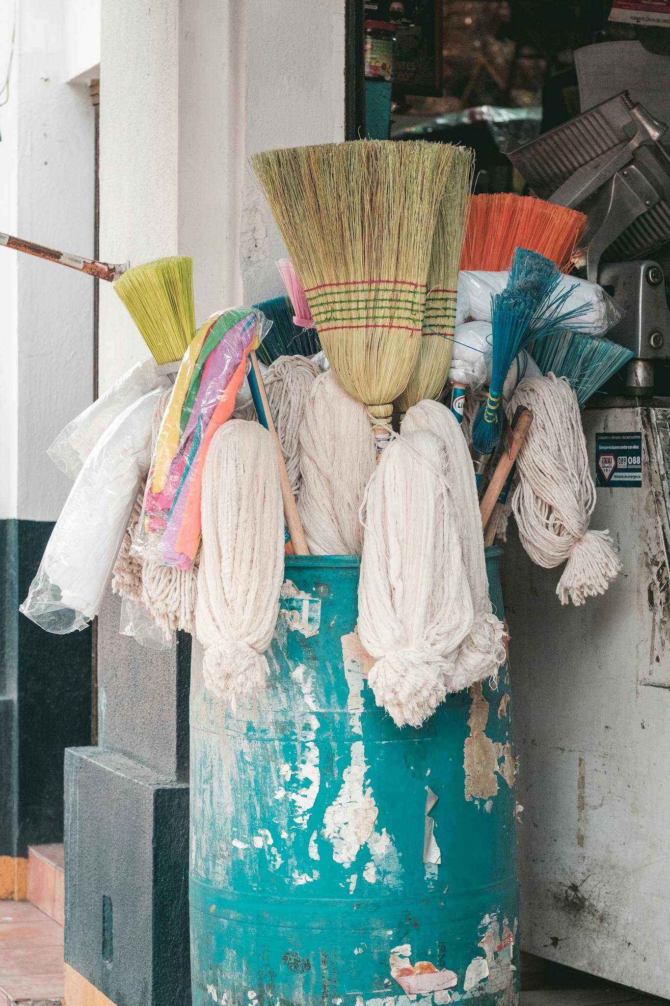 A vibrant display of brooms and mops in a rustic barrel outside a store entrance.